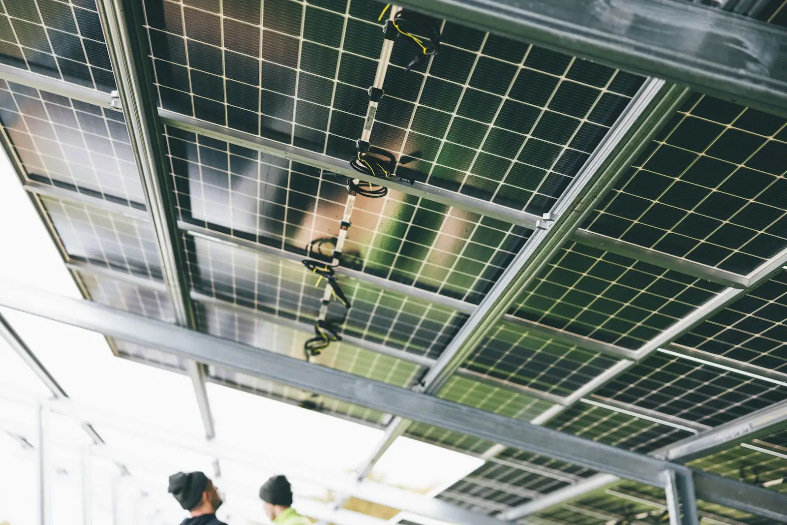 The underside of various ground-mounted solar panels, with two people stood underneath them.