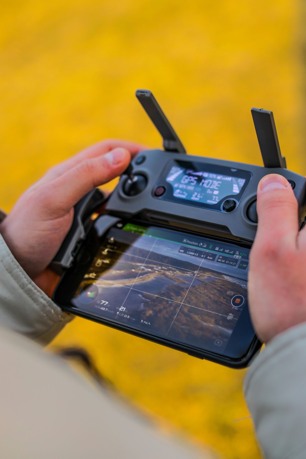 A close up of a man using a drone controller. His smart phone is attached to the controller and is showing what the drone can see.